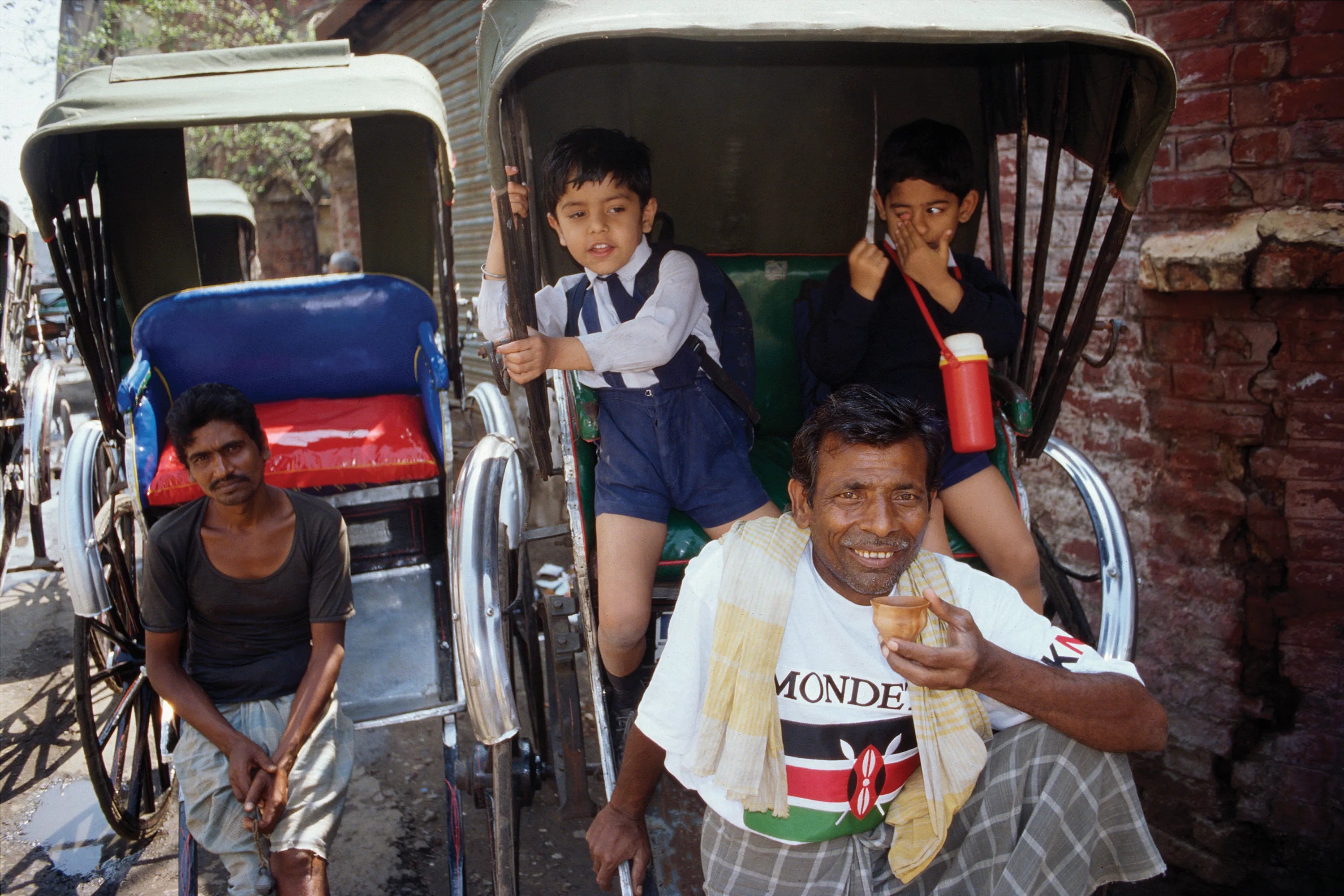 Bangladeshian family outside sitting in rickshaws with one man wearing a Mondetta Everywear Kenya t-shirt.