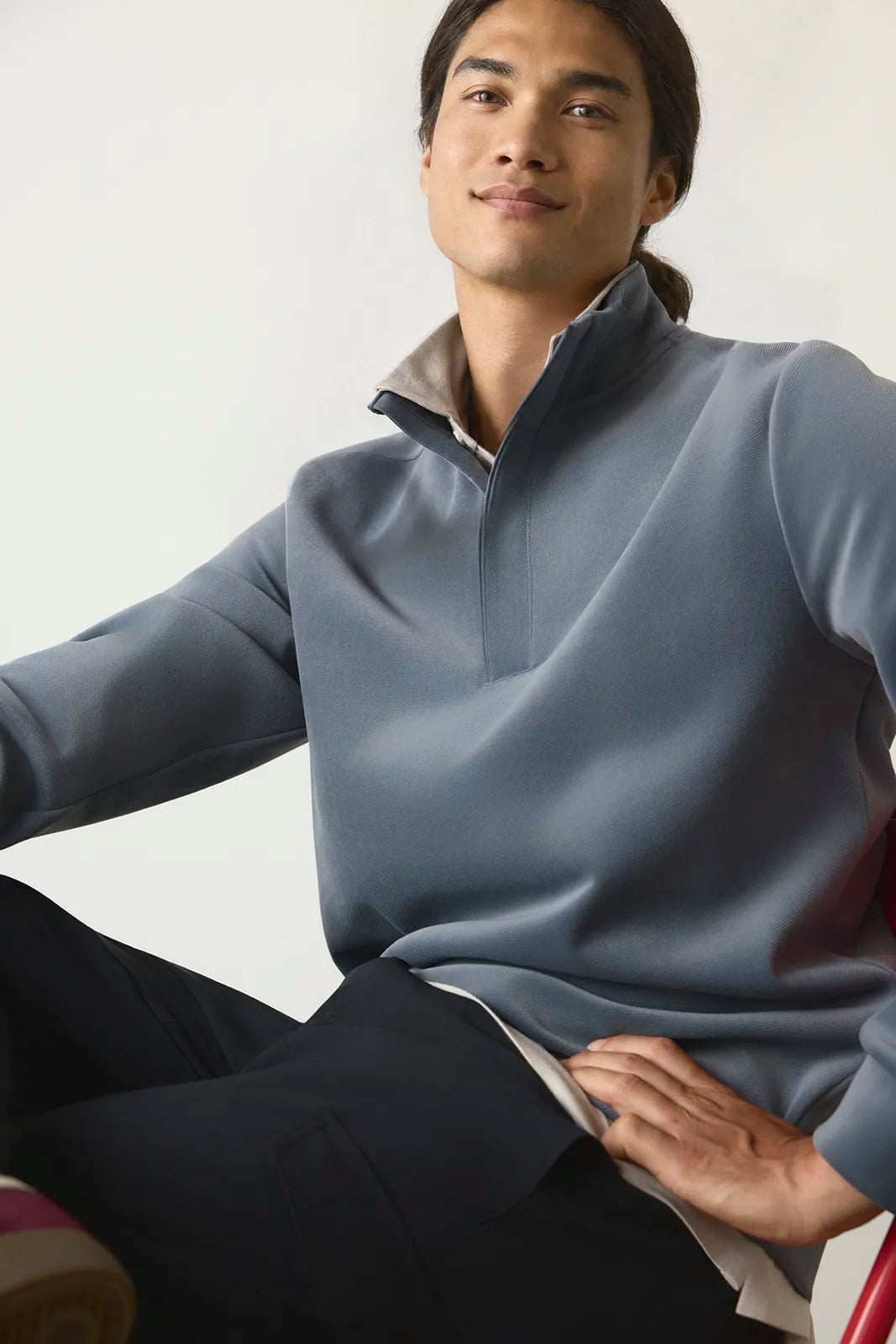A man wearing a slate blue quarter-zip pullover sweater with a contrasting light brown collar, seated against a plain light background.