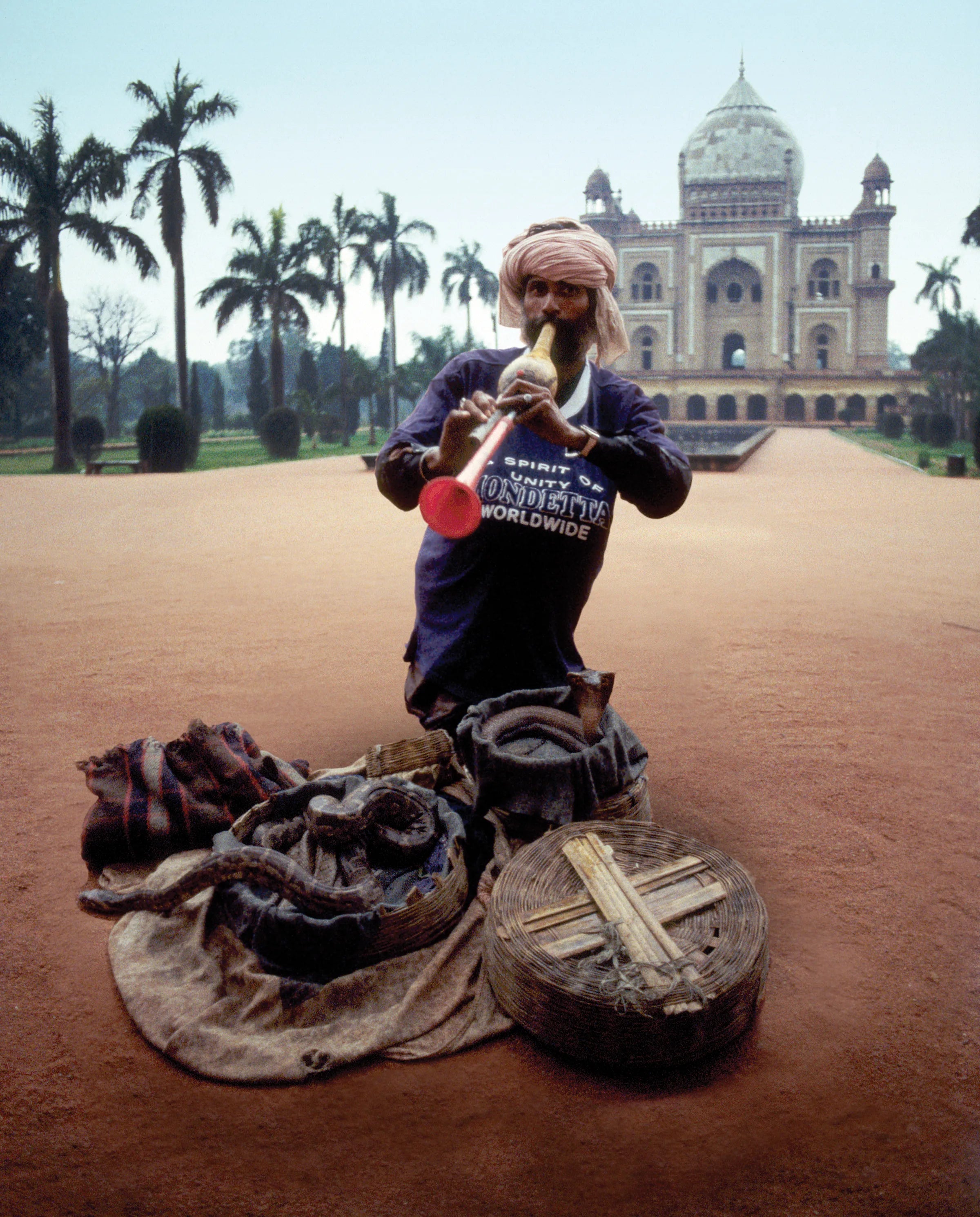 Indian man playing a pungi instrument sitting with baskets of snakes in front of the Taj Mahal, wearing a Mondetta sweatshirt