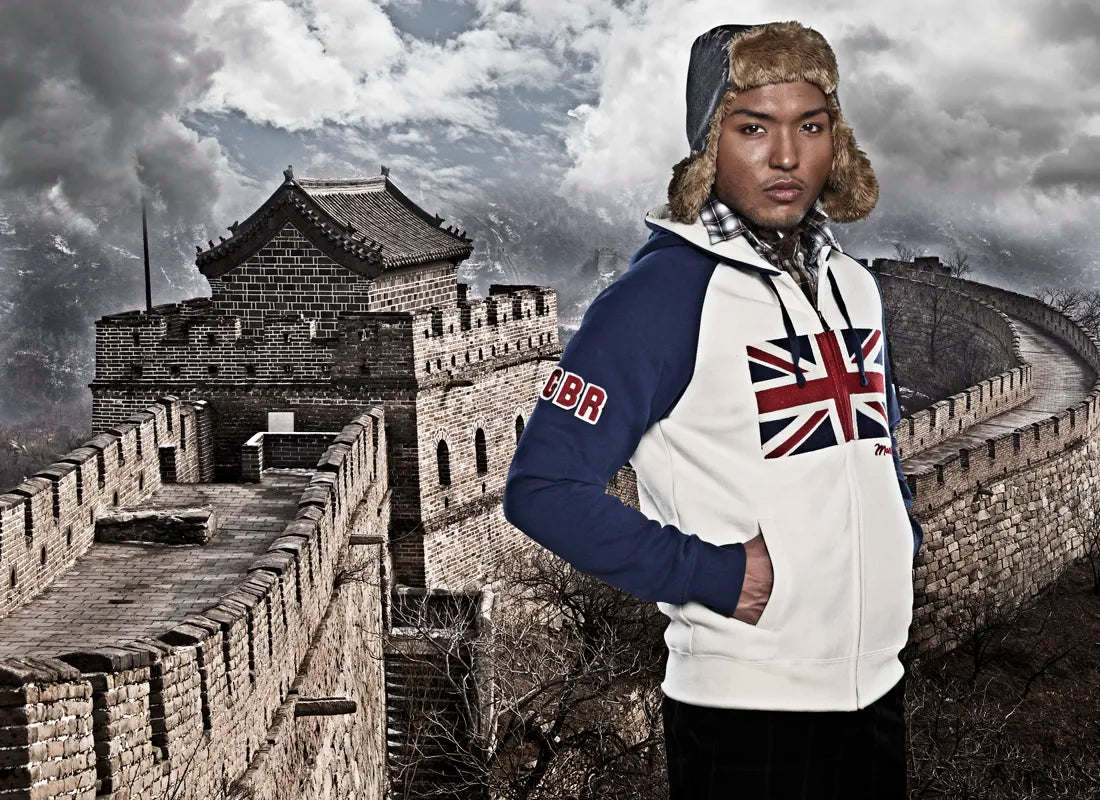 Asian man wearing blue/white Mondetta England flag zip-up sweater in front of a Great Wall of China backdrop.
