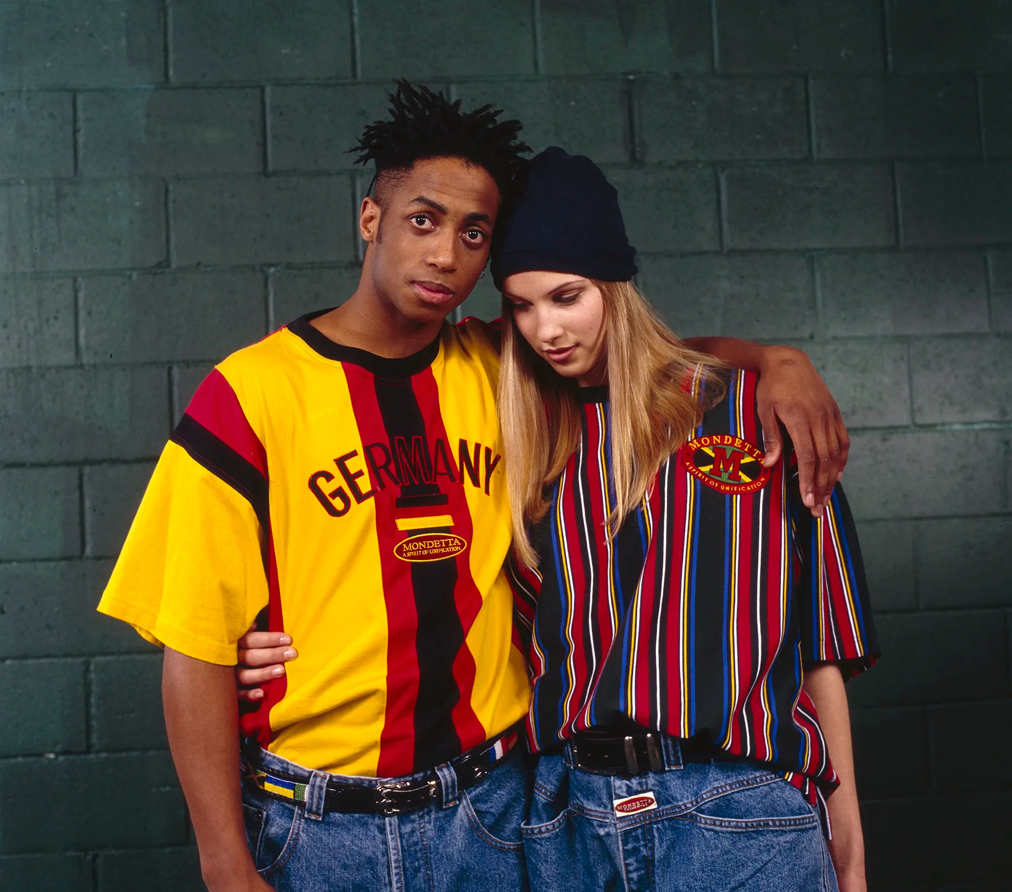 Black man and white woman with their arms around each other wearing brightly coloured Mondetta t-shirts.