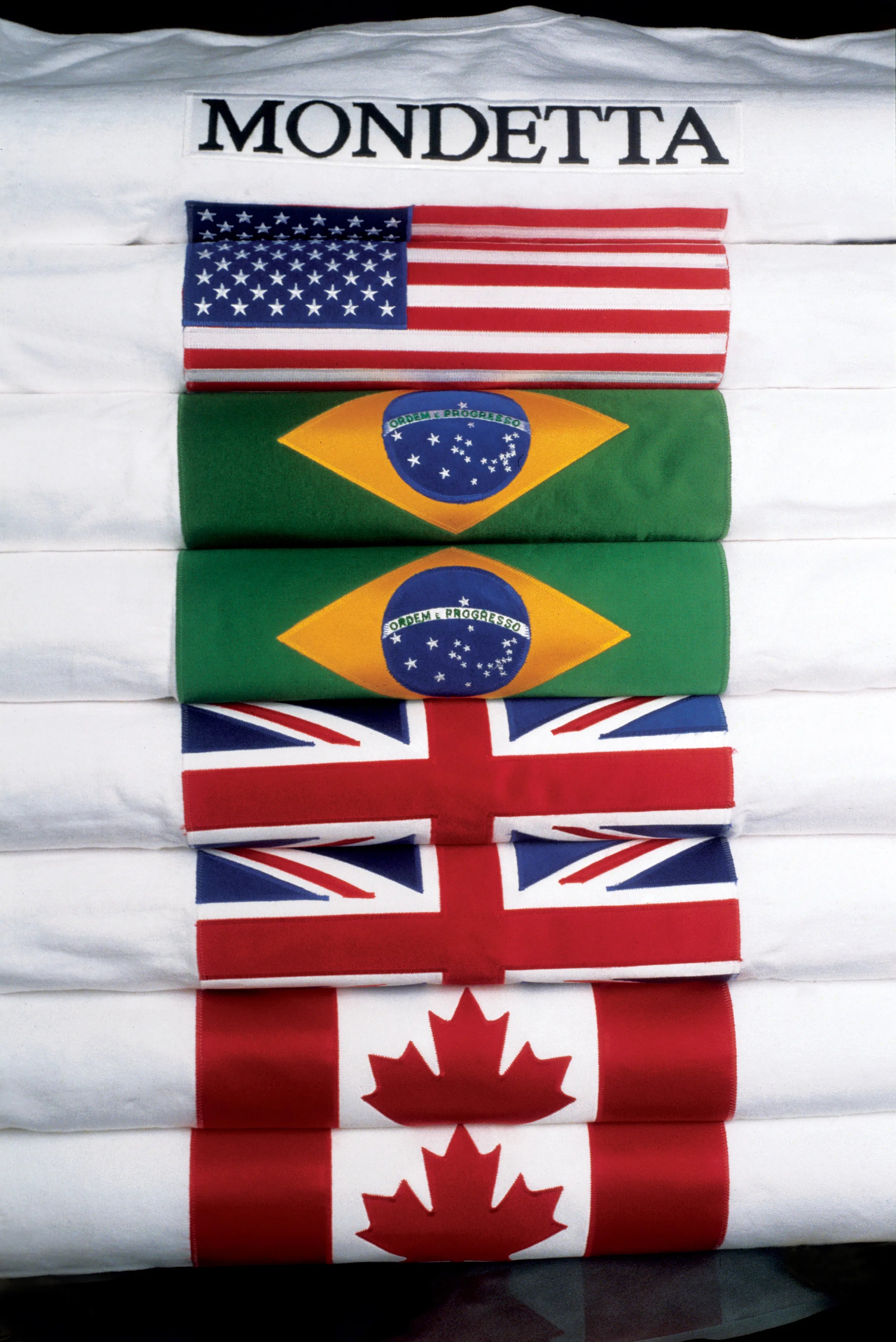 Stack of folded white Mondetta Everwear country flag sweatshirts featuring USA, Brazil, England, and Canada.