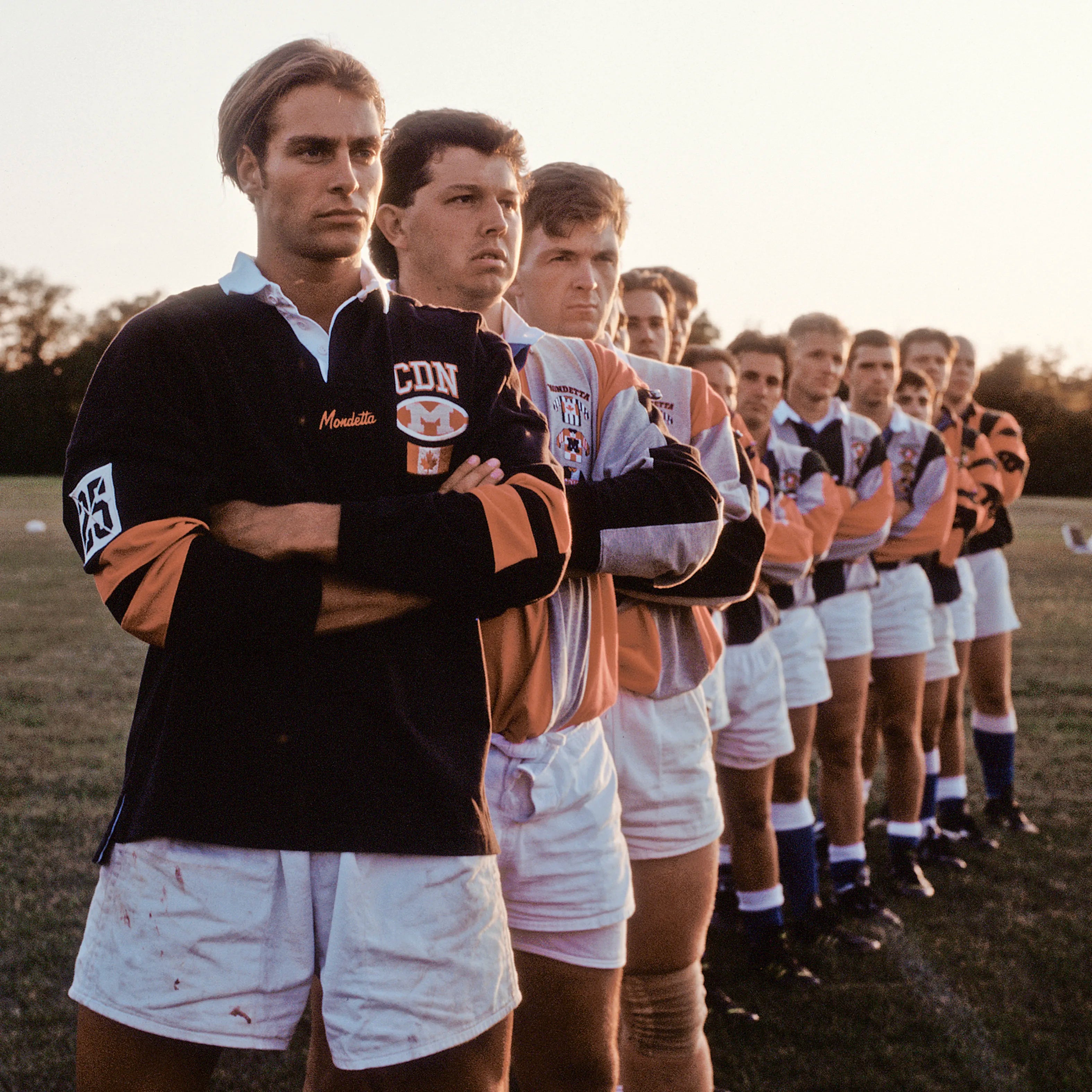 Vintage photo of rugby players in black and orange Mondetta uniforms standing in a lineup on a field.