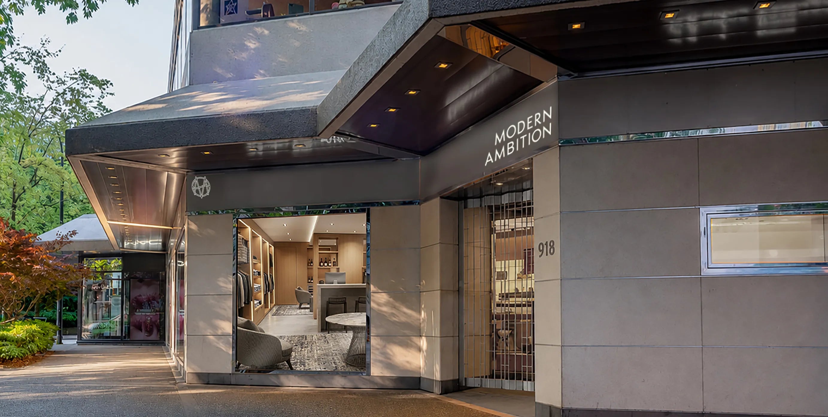 Inset storefront of a multi-floor building showing tall grey fascia under the roof overhang displaying glowing 'Modern Ambition' signage, with a big picture window showing the interior with seating.